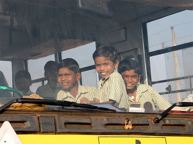 Children peer out a bus window in India. By marcusjroberts.